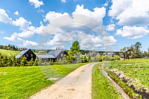 Sunny summer day in Jizerka mountain village. Dusty country road, green meadows and blue sky with white clouds, Jizera