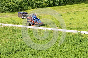 Sunny summer day.Mature man driving grass cutter in a sunny Gardener driving a riding lawn mower in a gardenay.Worker mowing grass