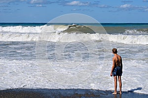 On a Sunny summer day, a teenager stands on the beach and watches the waves