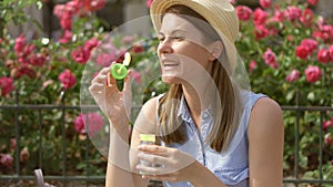 Sunny summer day. Young funny girl blowing air soap bubbles. Beautiful pink flowers on background