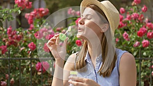 Sunny summer day. Young funny girl blowing air soap bubbles. Beautiful pink flowers on background