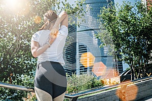 Sunny summer day. Young woman doing stretching exercises outdoor. Girl doing warm-up on steps before training.