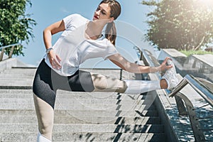 Sunny summer day. Young woman doing stretching exercises outdoor. Girl doing warm-up on steps before training.