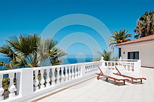 Sunny terrace with sun beds of ocean view house with palm trees anb blue sky copy space