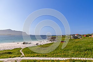 Sunny weather illuminates the pristine Jusnesvika Bay at Rambergstranda beach in Flakstadoya, Lofoten, with a couple heading for a