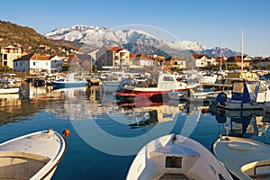 Sunny winter day. Fishing boats in harbor in Mediterranean town at foot of snowy mountains. Montenegro, Tivat city