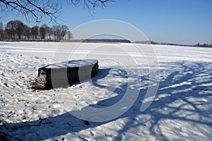 Sunny winter lake landscape with old boat and tree shadow