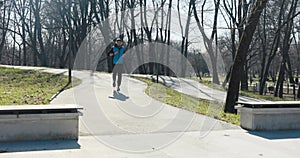 Sunny winter morning. Man runs in the park. He is dressed in black and blue sportswear and has cap and headphones on