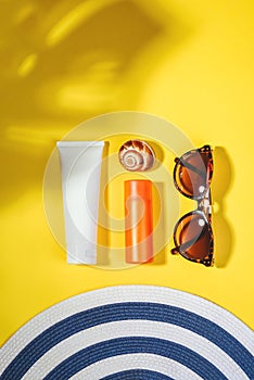Sunprotection objects. Hat with sunglasses and protection cream SPF Flat lay on yellow background. Beach accessories
