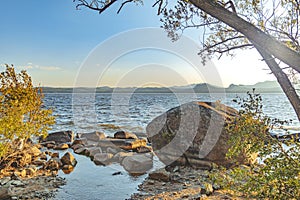 Sunray on background of large stones on seashore with mountains. Beautiful landscape of sea and mountains