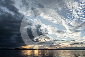 Sunrays at near sunset, with dark clouds in the background, above Trasimeno lake Umbria, Italy