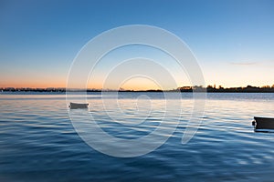 Sunrise across bay with small dinghy blue tones with orange around horizon