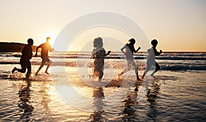 Sunrise, beach and friends with freedom, running and having fun in water together on summer vacation. Ocean, silhouette
