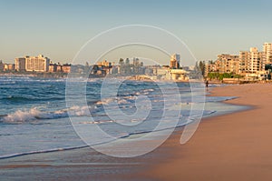 Sunrise beach seascape with unrecognizable surfer and cityscape in the distance