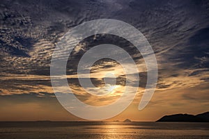 sunrise from behind golden cumulus clouds above sea and island