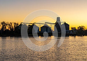 Sunrise behind large grain storage bins by Mississippi River