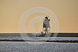 Sunrise behind lighthouse at dawn with soft golden sky and Lake Michigan water in ocean endlessness