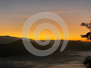 Sunrise behind mountain in the morning with magnificent mist landscape in winter season.