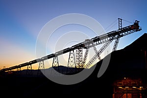 Sunrise behind silhouetted stockpile and conveyor belt in a copper mine at the Atacama Desert