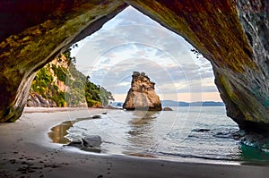Sunrise at Cathedral Cove with blue sky with white clouds above and refelction in the sea, golden hour