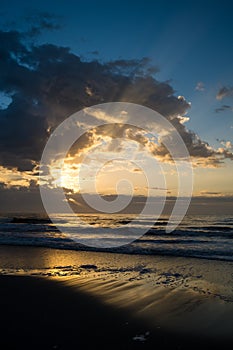 Sunrise with Clouds and Beams of Light Over the Beach and Ocean