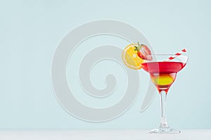 Sunrise cocktail with red and yellow liquor, orange slice, strawberry, straw on elegant white wood board and pastel mint color.
