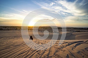 Sunrise in desert. Scene with two ATV bikers. Tourists ride on an off-road ATV through the sand dunes of the Vietnamese