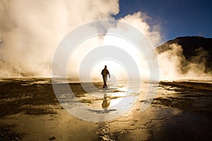 Sunrise at El Tatio Geysers with a tourist walking between the fumaroles in the Atacama desert, Chile