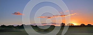 sunrise with glowing clouds over a wide rural landscape with meadows and trees in the morning mist, panorama format with copy spa