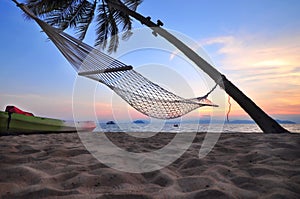 Sunrise with hammock and coconut palm trees on tropical beach background