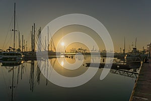 Sunrise in the harbor of Valencia, the sun rises between docked sailboats and cargo port cranes