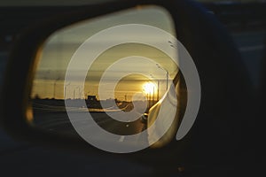 Sunrise on highway road in left side view mirror driver. Focus on reflection in smaller mirror.