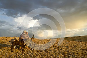 Sunrise hunter and dogs in moody arid landscape