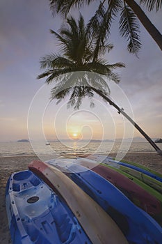 Sunrise with kayak boat and coconut palm trees on tropical beach background