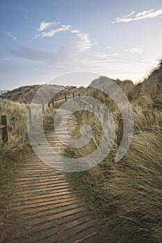 Beautiful sunrise landscape image of sand dunes system over beach with wooden boardwalk