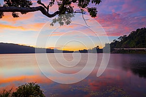 Sunrise landscape. Lake surrounded by mountains and hills. Colorful sky. Amazing water reflection. Nature background. Foreground