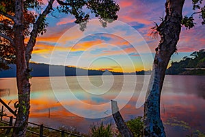 Sunrise landscape. Lake surrounded by mountains and hills. Colorful sky. Amazing water reflection. Nature background. Foreground