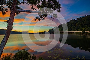 Sunrise landscape. Lake surrounded by mountains and hills. Colorful sky. Amazing water reflection. Nature background. Foreground