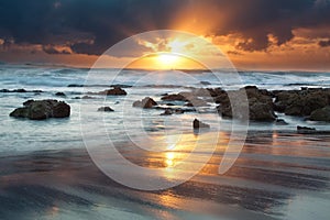 Sunrise landscape of ocean with waves clouds and rocks