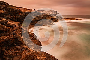 Sunrise landscape of ocean with waves clouds and rocks