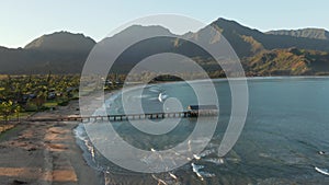 Sunrise lights the mountains as drone descends to ocean while facing the on Hanalei bay on hawaiian island of kauai