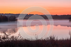 sunrise, with mist hovering over still lake, and orange and pink hues on the horizon