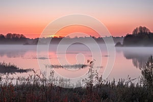 sunrise, with mist hovering over still lake, and orange and pink hues on the horizon