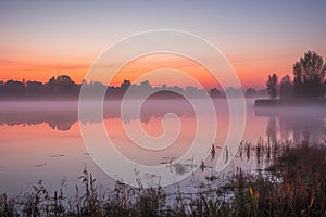 sunrise, with mist hovering over still lake, and orange and pink hues on the horizon