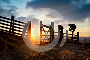 Sunrise in mountain hills hiker climber climbing over wooden fence style silhouette with open gate sun rising over countryside.