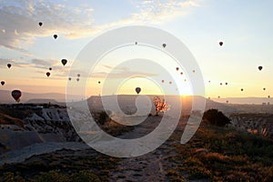 The sunrise in the mountains with a lot of air hot balloons in the sky.