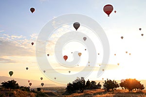 The sunrise in the mountains with a lot of air hot balloons in the sky.