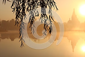 Sunrise near church and lake. fog over the water. a look through the willow branches at dawn