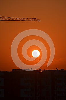 Sunrise orange coloured sky Sun clouds. Buildings silhouette photography black Crane machinary. Construction site foreground.