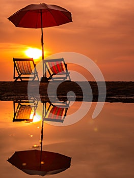 Sunrise with orange morning sky with chair and umbrella on beach reflection in water